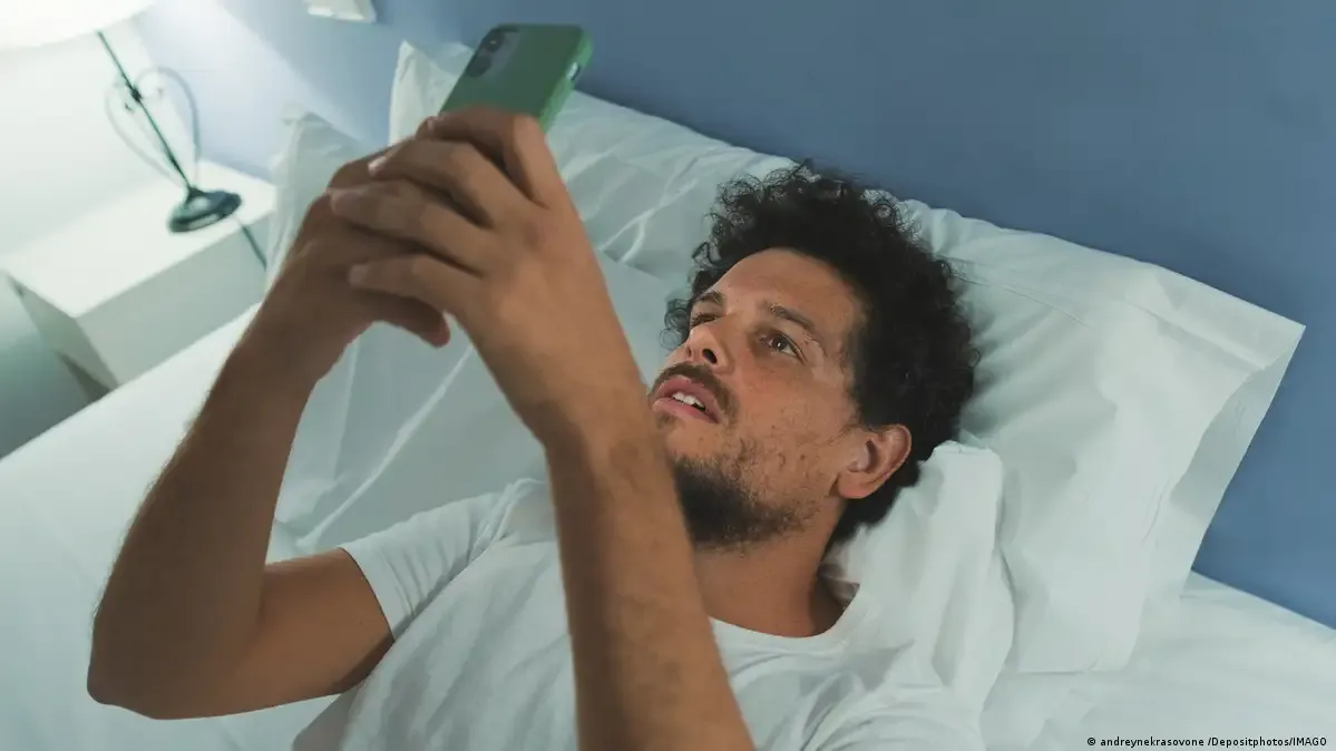 Un hombre mira el teléfono móvil en la cama durante la noche